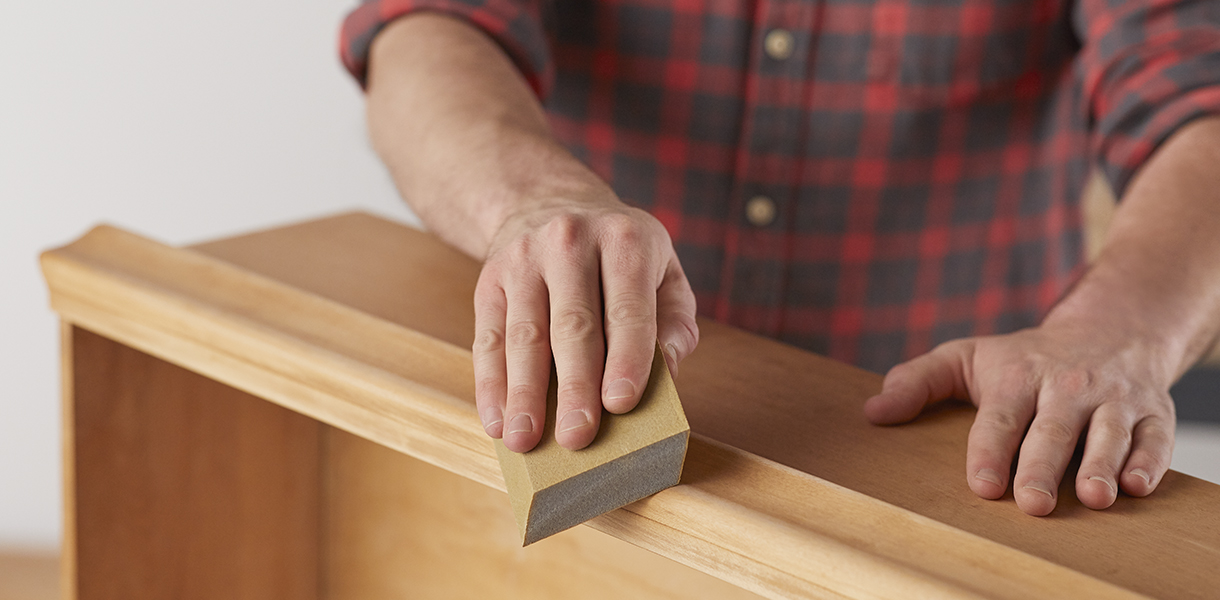 A man in a plaid shirt applies Wipe-On Polyurethane, after Minwax Antique Refinisher, to a dresser.